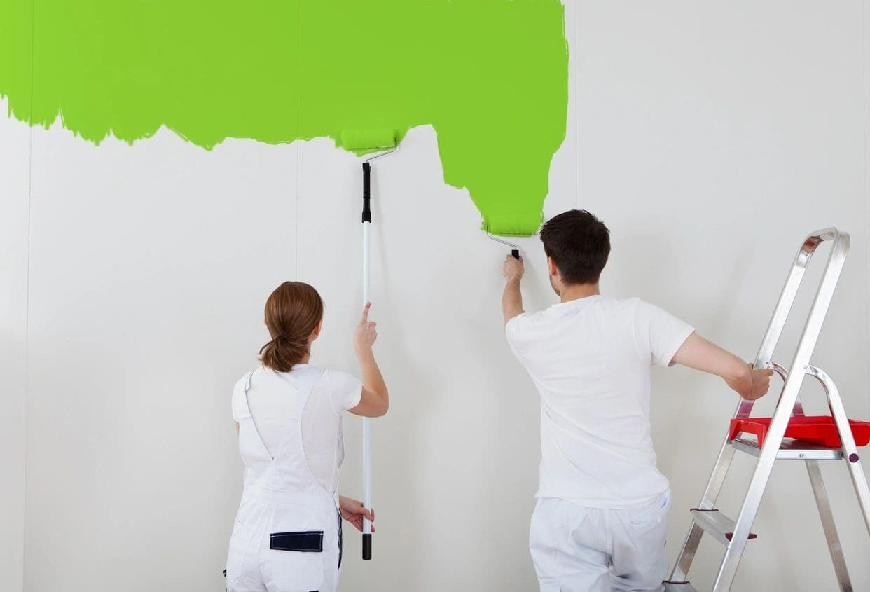 A man and woman painting the wall green.